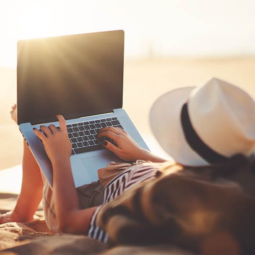 woman-on-beach-with-laptop-best-places-for-girl-trips